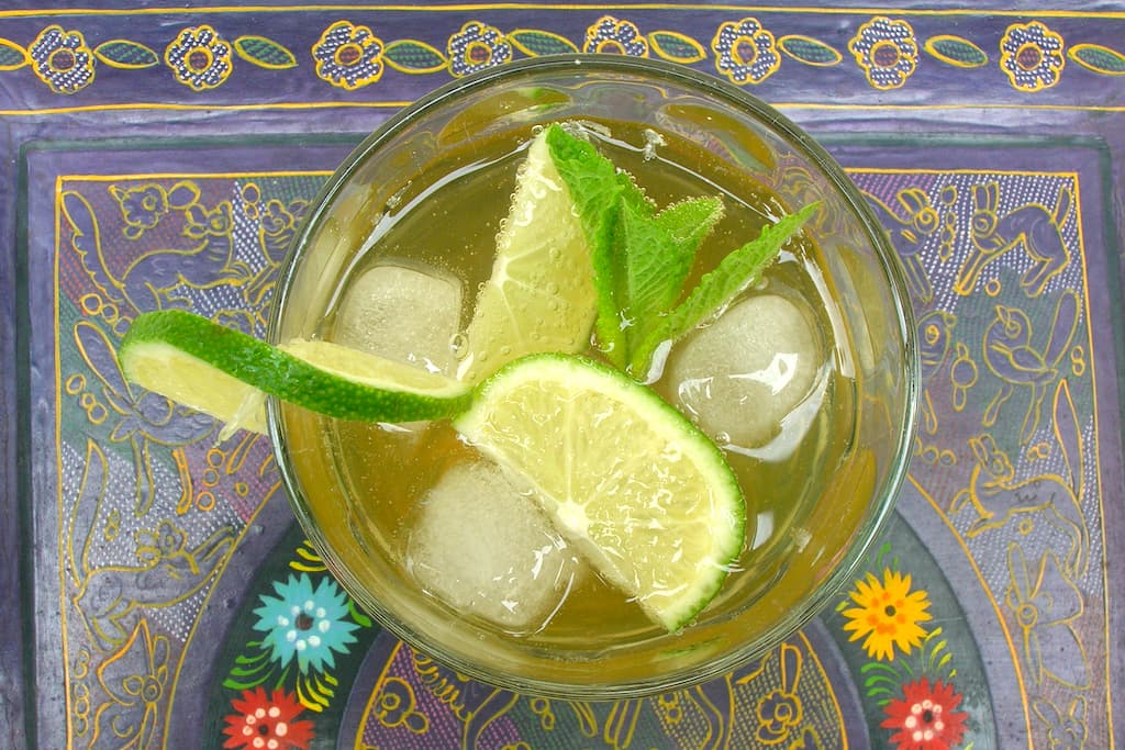 A mojito cocktail with lime and mint served on a purple Mexican tray.