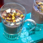 Two glasses of honeyed rose hot chocolate topped with crunchy nuts.