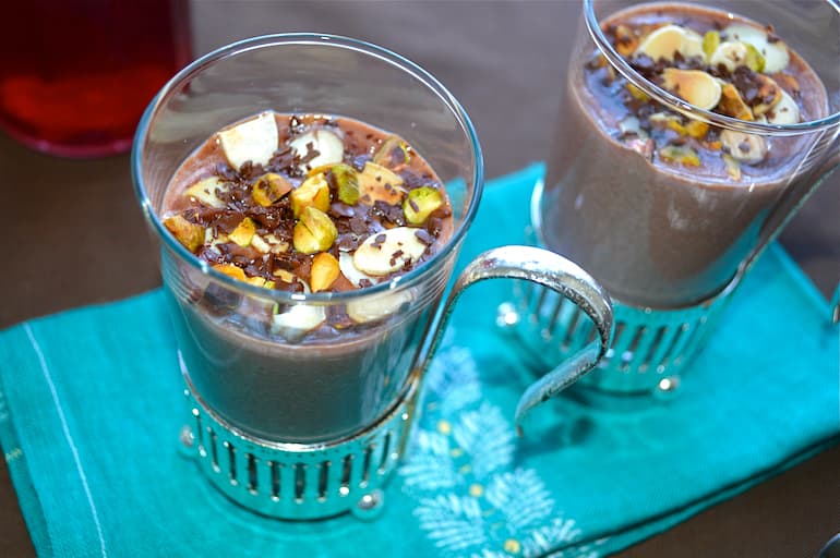 Two glasses of honeyed rose hot chocolate topped with crunchy nuts.