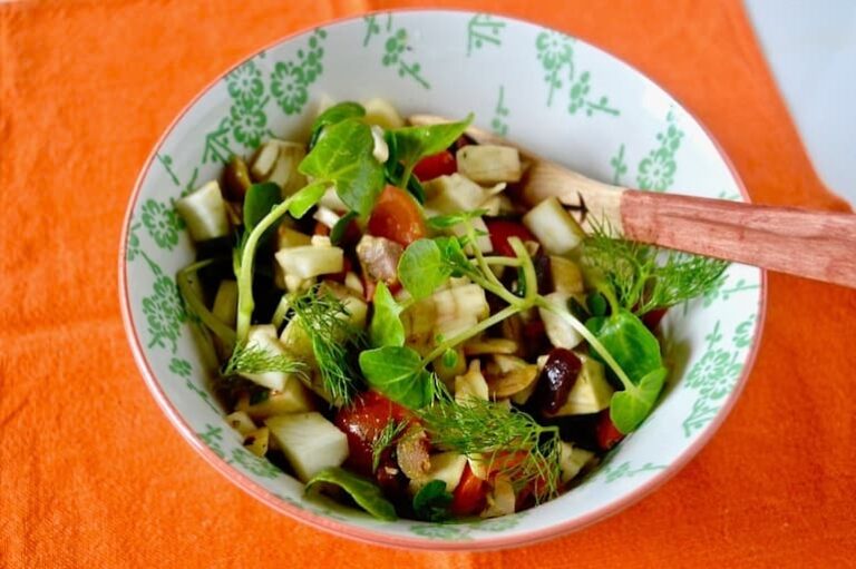A bowl of bulb fennel salad on an orange cloth with spoon.