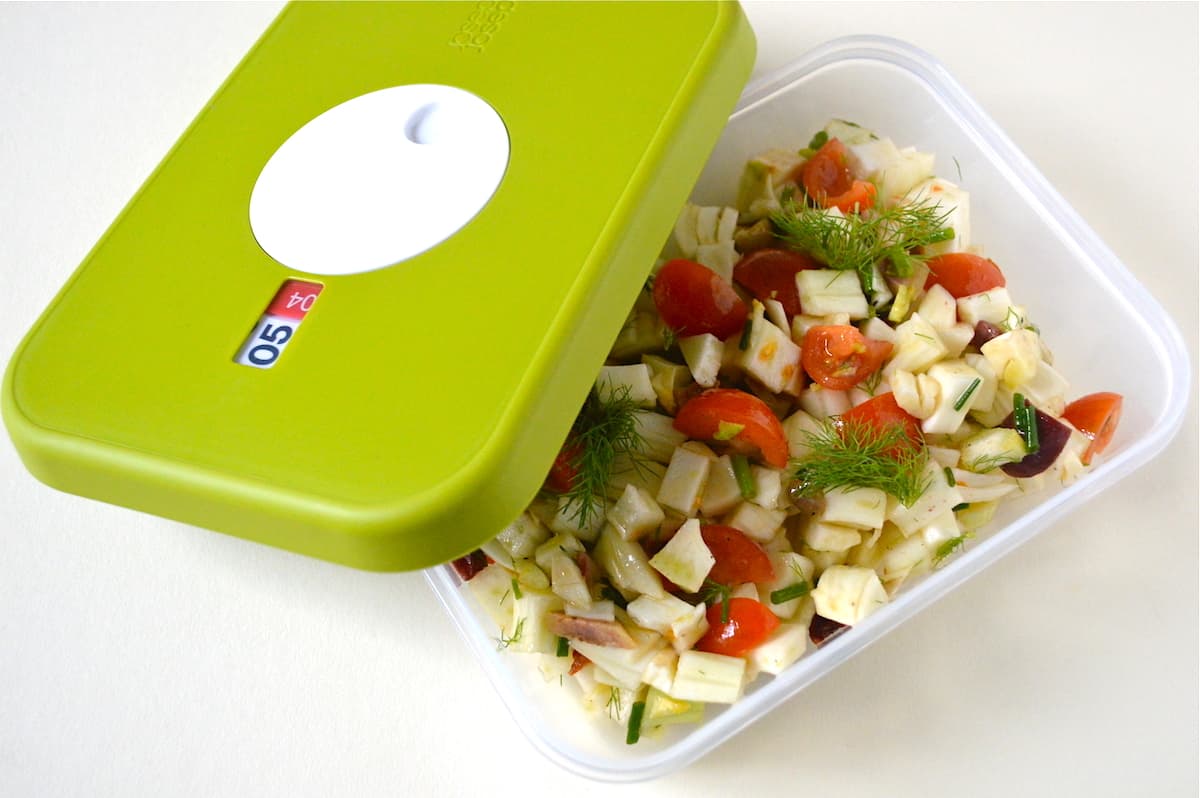 A food container of fennel salad with green lid on the side.