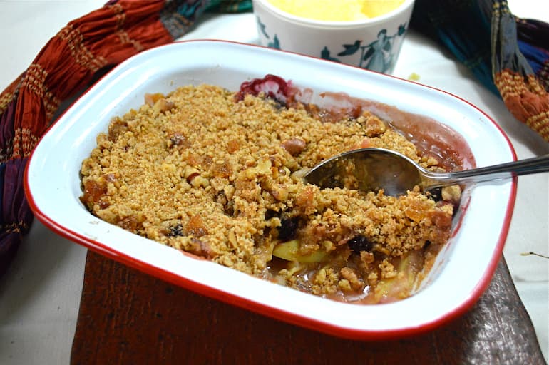 Blackberry and apple crumble in baking dish with serving spoon.