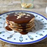 A stack of wholemeal spelt pancakes on a plate with chocolate sauce.