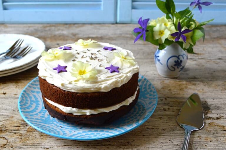 Iced lavender honey cake decorated with fresh primroses on blue plate.