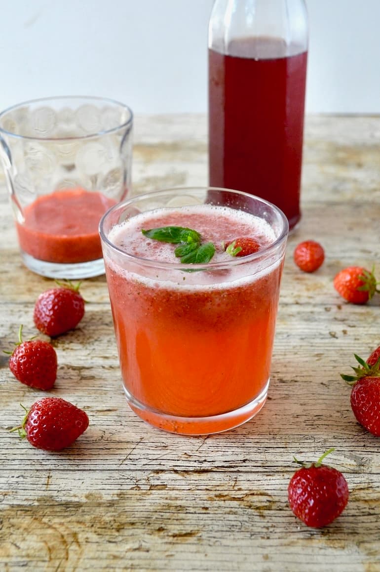Glass of homemade strawberry rose mint fizz with strawberries and bottle of rose syrup.
