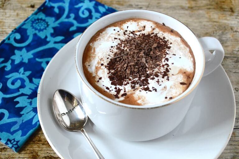 A mug of real hot chocolate topped with marshmallow fluff and grated chocolate.