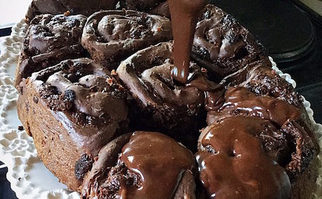 Chocolate sauce pouring over a plate of double chocolate chip buns.