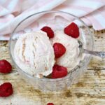 Peach Melba ice cream in a bowl with spoon and raspberries.