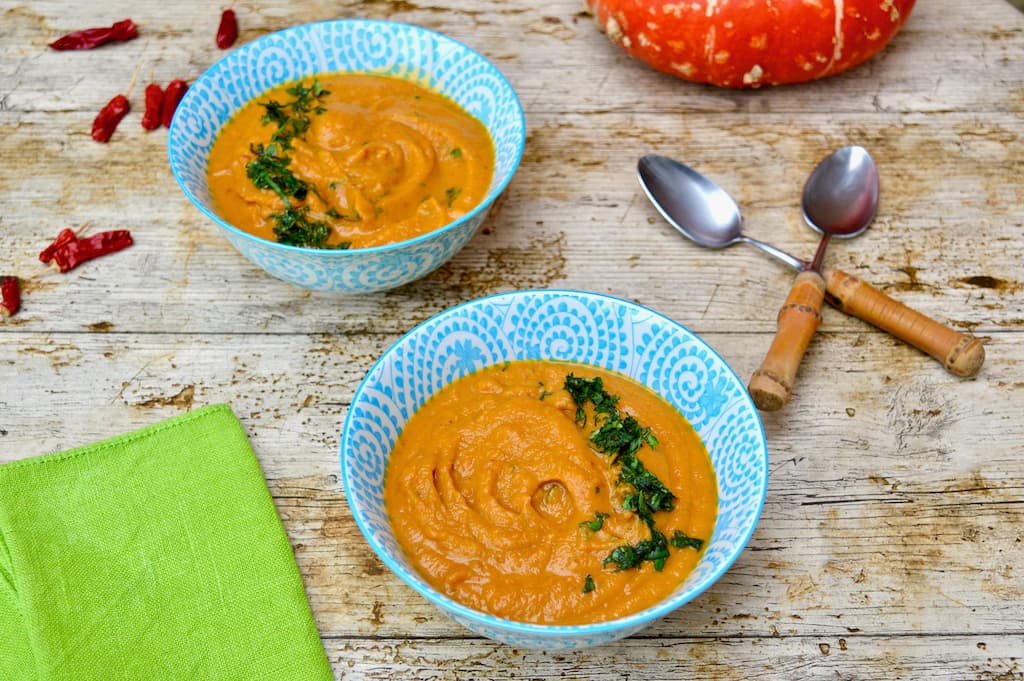 Two blue bowls of orange sweet potato and carrot soup.