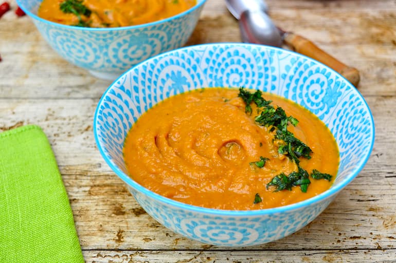 A blue bowl of orange sweet potato & carrot soup.