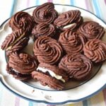 Plate of chocolate Viennese whirls sandwiched with blackcurrant jam and vanilla buttercream.