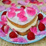 Raspberry Cream Sponge Cake scattered with fresh raspberries and rose petals.