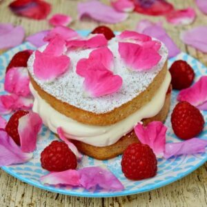 Raspberry Cream Sponge Cake scattered with fresh raspberries and rose petals.