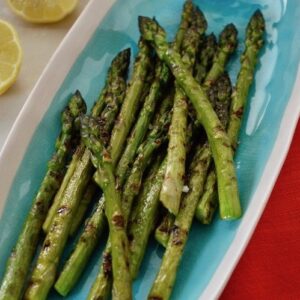 Turquoise serving plate with griddled asparagus, lemon halves with napkins and forks at the ready.