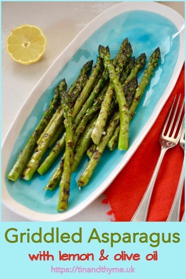 Griddled asparagus on a turquoise serving platter with lemon, forks and a red napkin.