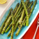Turquoise serving plate with griddled asparagus, lemon halves, napkins and forks on the sides.