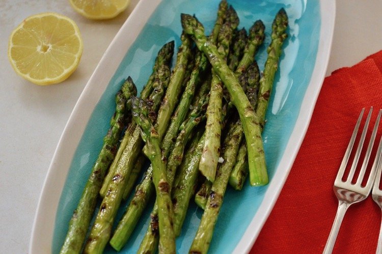 Turquoise serving plate with griddled asparagus, lemon halves with napkins and forks at the ready.