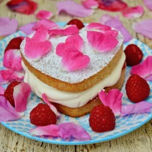 Raspberry Cream Sponge Cake scattered with fresh raspberries and rose petals.