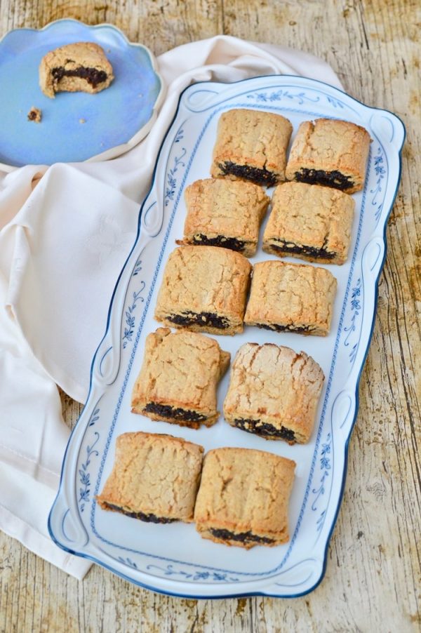 Platter of fig rolls with a half eaten one on a blue plate.