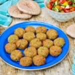 Homemade fava bean falafel on plate with chopped salad and pitta breads.