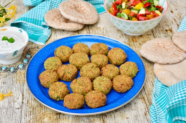 Homemade fava bean falafel on plate with chopped salad and pitta breads.