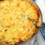 Vegetarian lentil shepherd's pie just out of oven with serving spoon inserted.