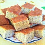 Lemon and poppy seed traybake cut into squares and piled on a plate.
