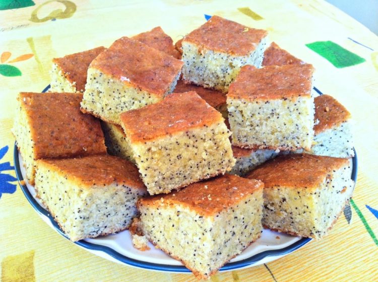 Lemon and poppy seed traybake cut into squares and piled on a plate.
