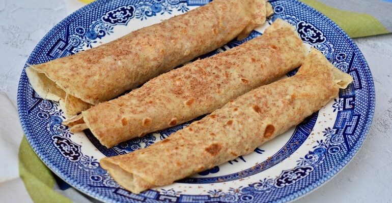 Three rolled chocolate, honey and cream pancakes on a plate.