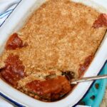 Homemade rhubarb crumble in enamel pie dish with spoon.