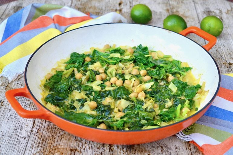 Pan of spinach coconut curry with napkins and limes in the background.