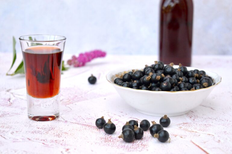 Glass of easy homemade cassis with a bowl of blackcurrants.