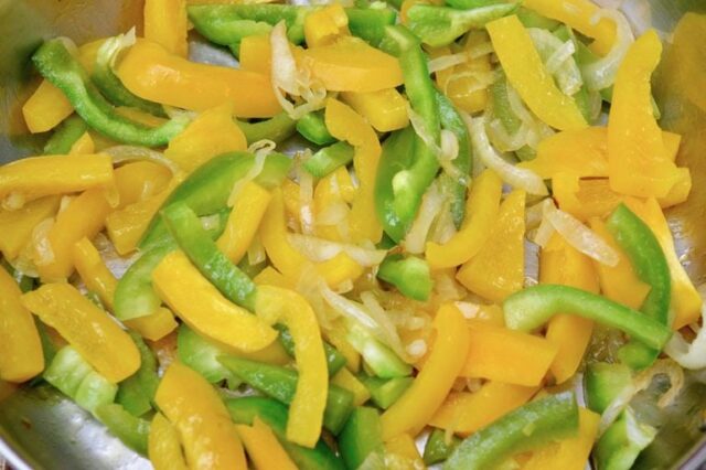 Slided peppers and onions frying in a pan.
