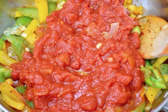 Sliced peppers and chopped tomatoes cooking in a pan.