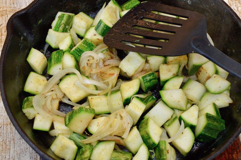 Courgettes and onions frying in a pan.