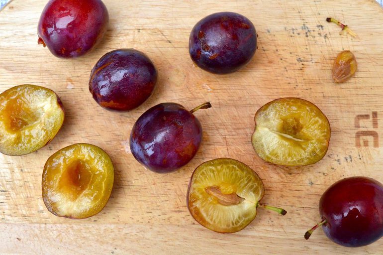 Purple plums on a board. Some whole, some halved.