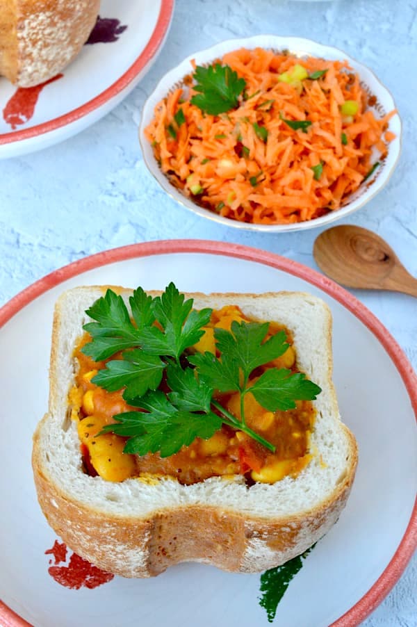 Beany Bunny Chow - Vegan Curry in a Bread Basket with a bowl of grated carrot salad on the side.