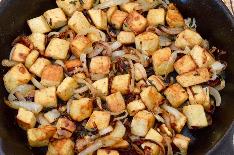 Onions and tempeh cubes frying in a cast iron pan.