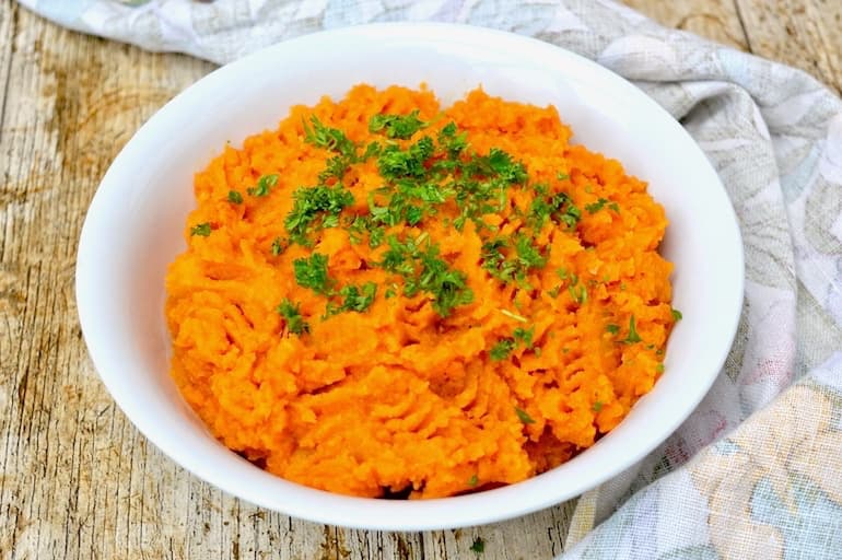 A bowl of carrot and swede mash with a scattering of parsley.