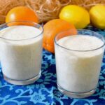 Two glasses of orange kefir smoothie with oranges and lemons in the background.
