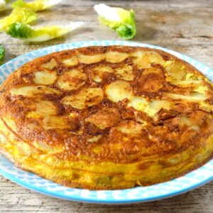 A whole easy Spanish tortilla on a blue plate with lettuce leaves in the background.