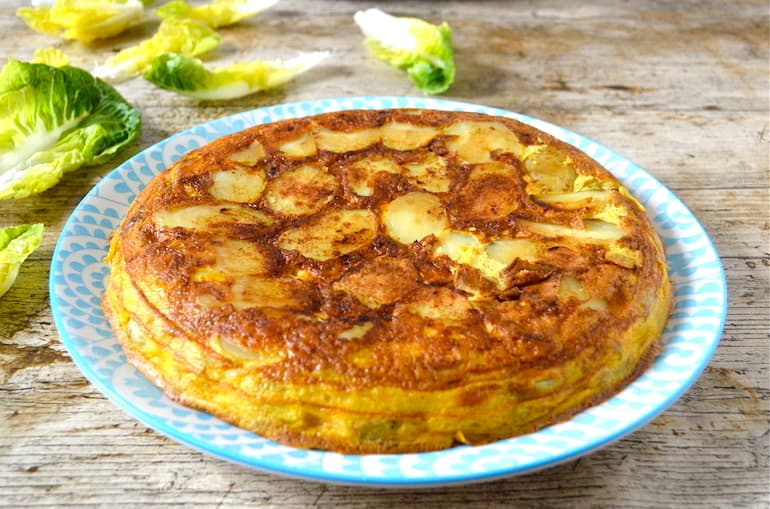 A whole easy Spanish tortilla on a blue plate with lettuce leaves in the background.