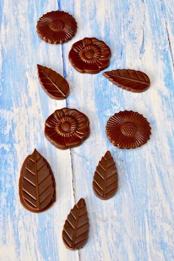 Flower and leaf shaped homemade mint chocolates laid out on a blue board.