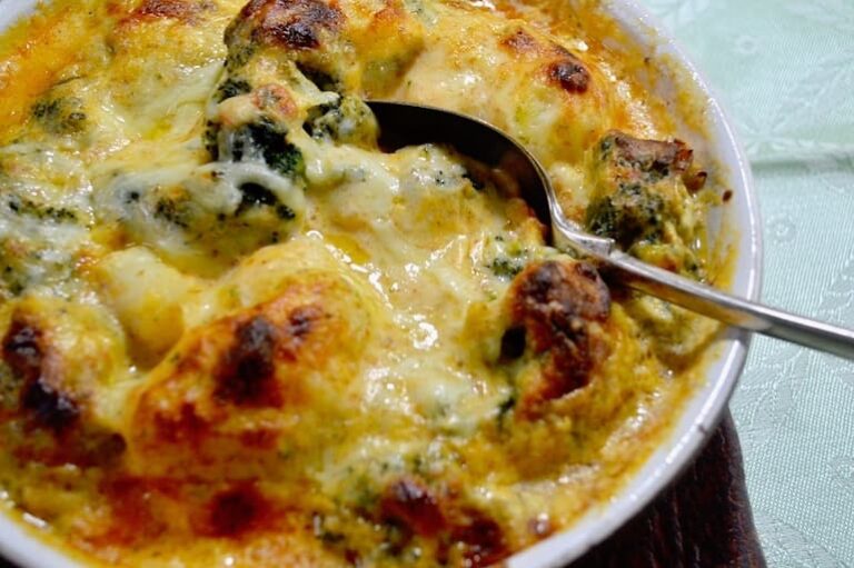 A dish of broccoli cauliflower cheese with serving spoon embedded.