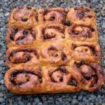 Chocolate Chelsea buns on a cooling rack siting outside on some gravel.
