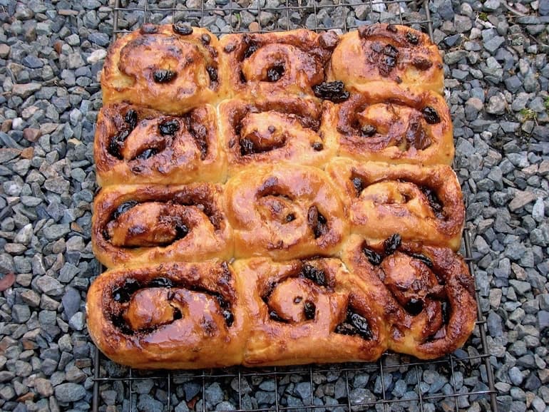 Chocolate Chelsea buns on a cooling rack siting outside on some gravel.
