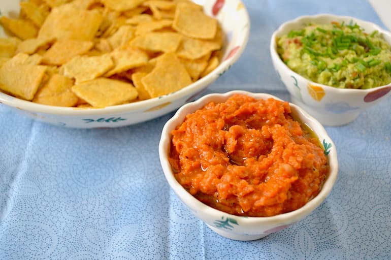 Red pepper and bean dip with a bowl of chips and a bowl of guacamole.
