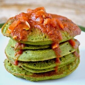 A stack of green kefir kale pancakes topped with tomato sauce.