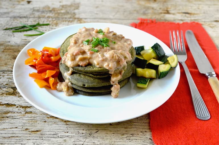 Pea Stack of pea protein pancakes with peanut sauce and roast vegetables on a white plate.