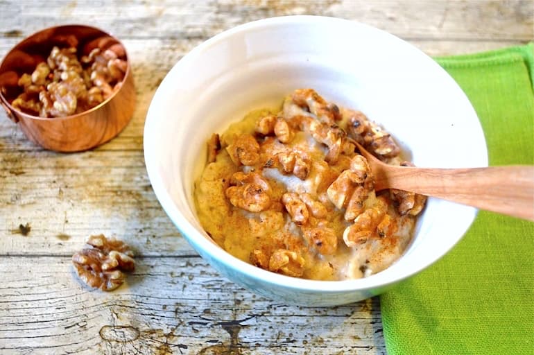 Bowl of prune porridge topped with toasted walnuts and cinnamon.